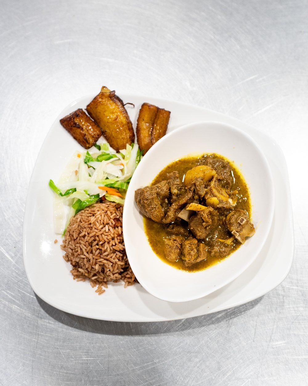 Curry goat with rice and peas, cabbage, and plantains