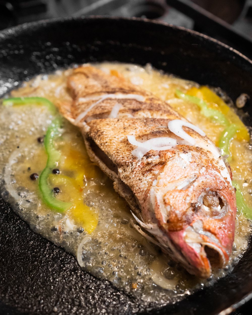 Whole fried fish with peppers and onions in a sizzling pan
