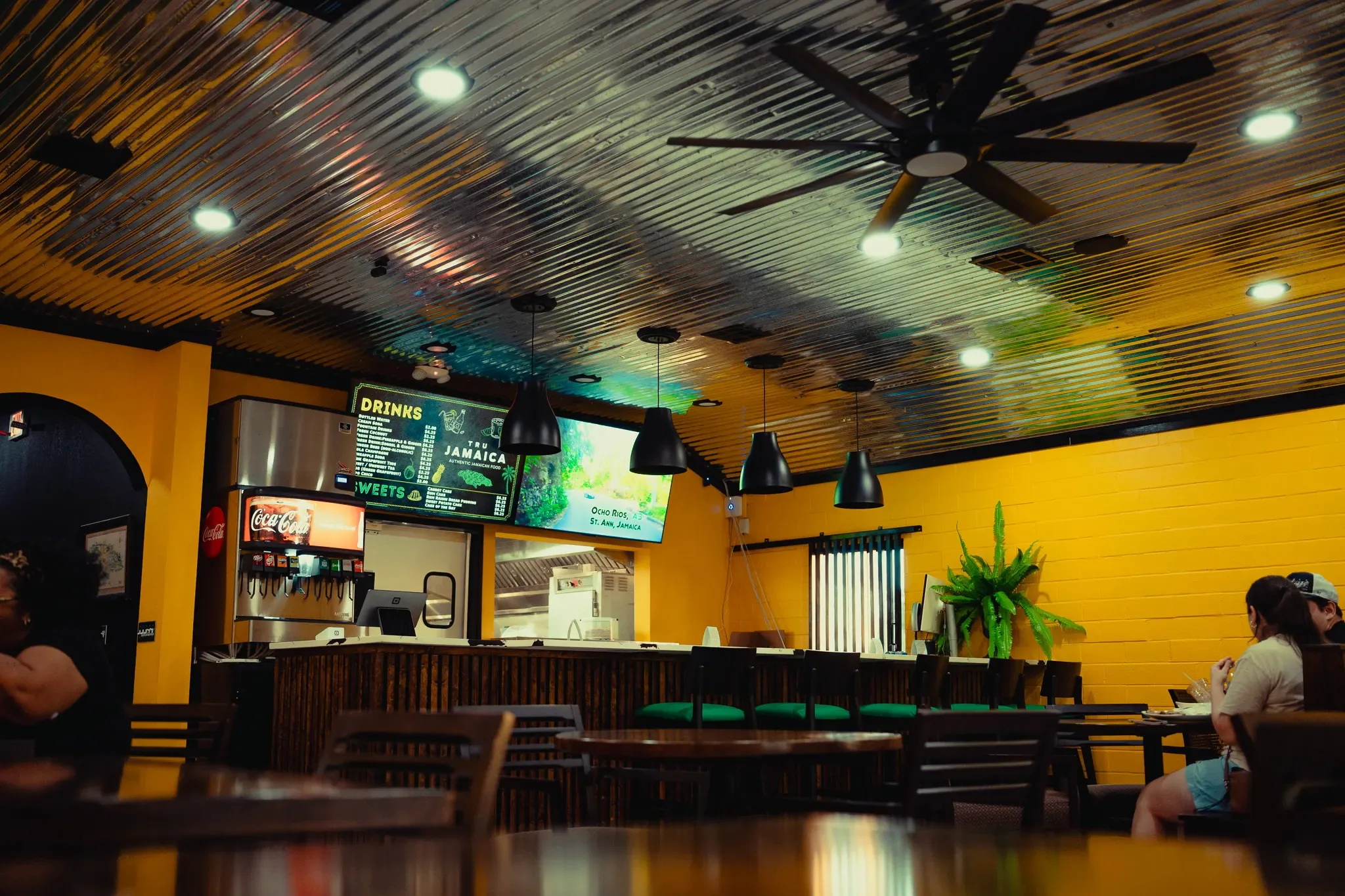 The Tru Jamaica dining room with yellow walls, a wood bar and pendant lights