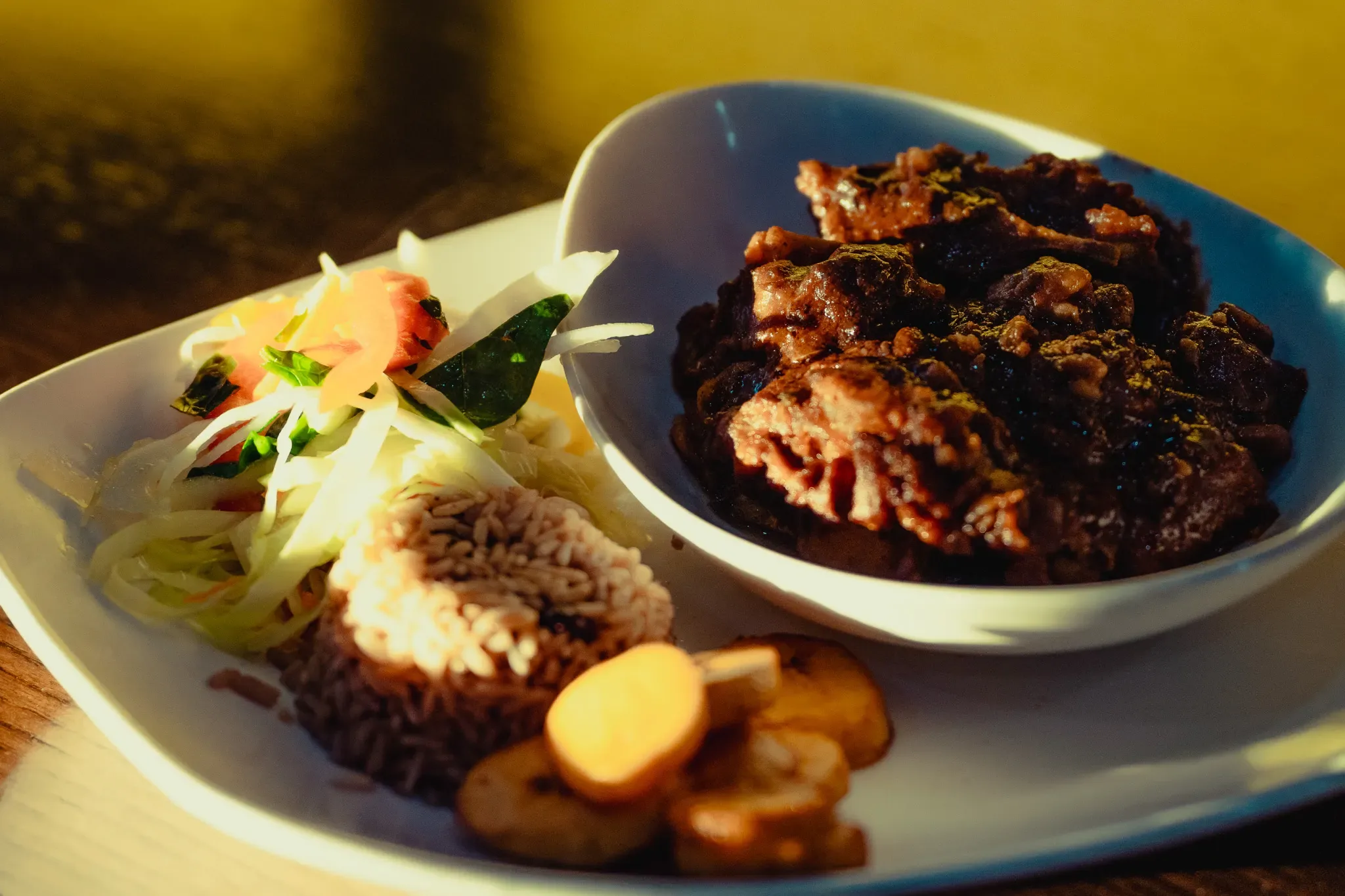 Oxtail with rice and peas, cabbage and fried plantain in warm evening light