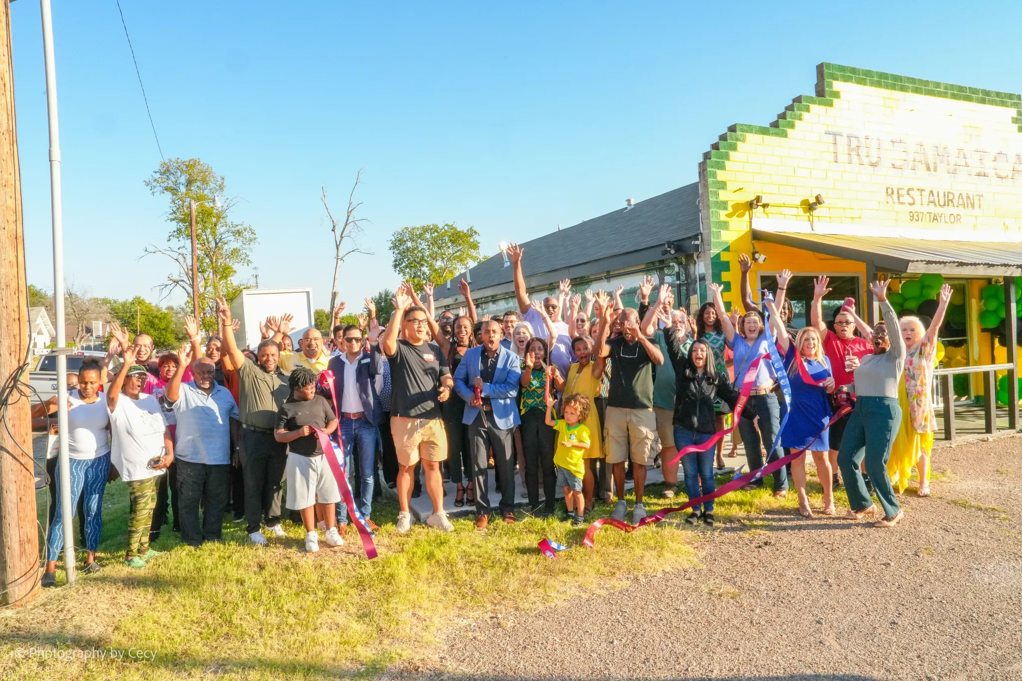 A crowd cheering with arms raised at the ribbon cutting in front of the new Tru Jamaica building